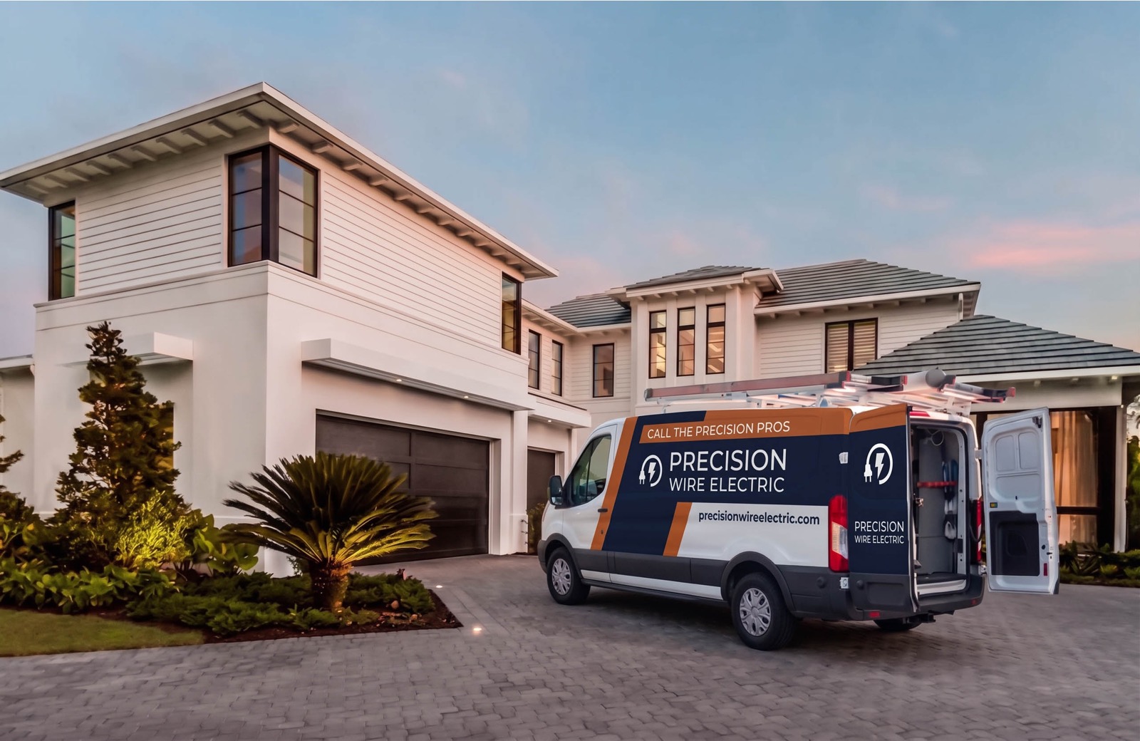 A Precision Wire Electric service van parked on the driveway of a modern two-storey home at dusk.