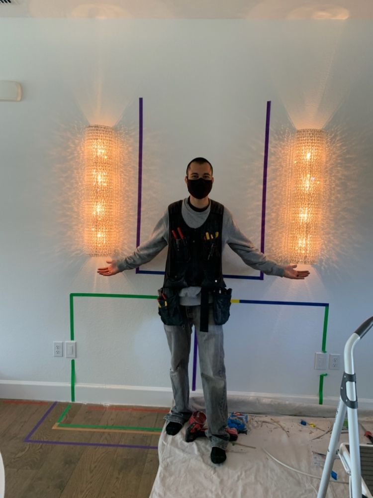 An electrician standing between two newly installed decorative wall sconces, layout still taped out on the wall.