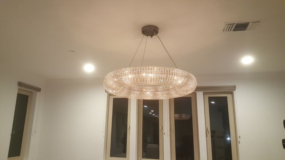 A crystal ring chandelier hung and energized over a dining room, with recessed lighting balanced around it.