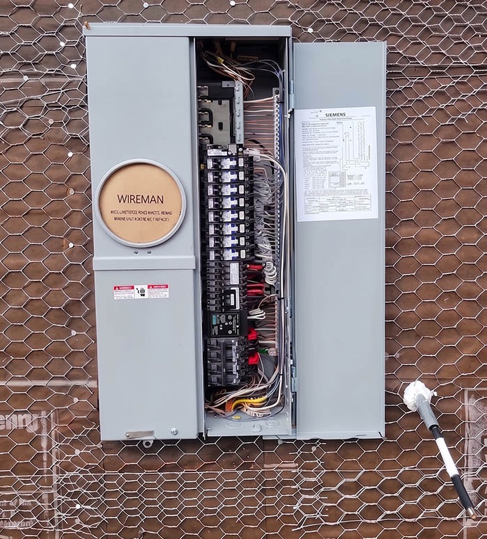 An open meter-main service panel on an exterior wall at rough-in, breakers installed and conductors dressed and terminated.