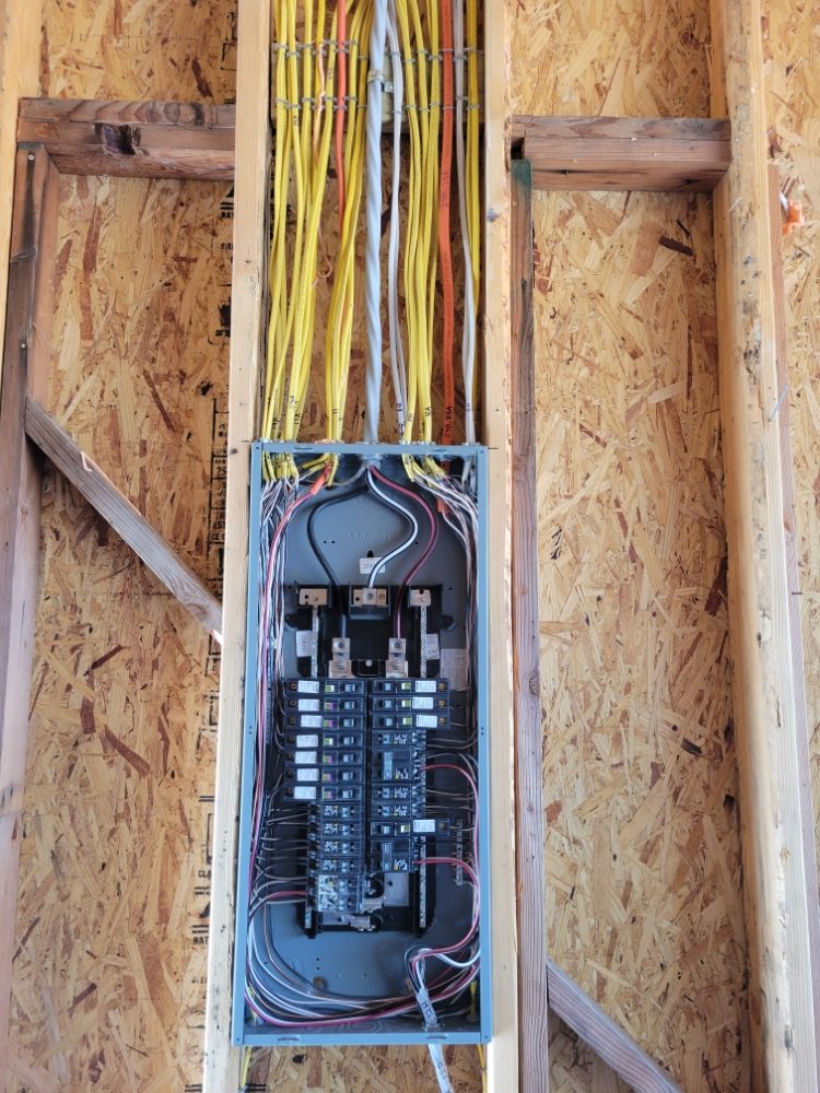 Sub-panel set into open framing at rough-in, home runs stapled and dressed in neat parallel rows.