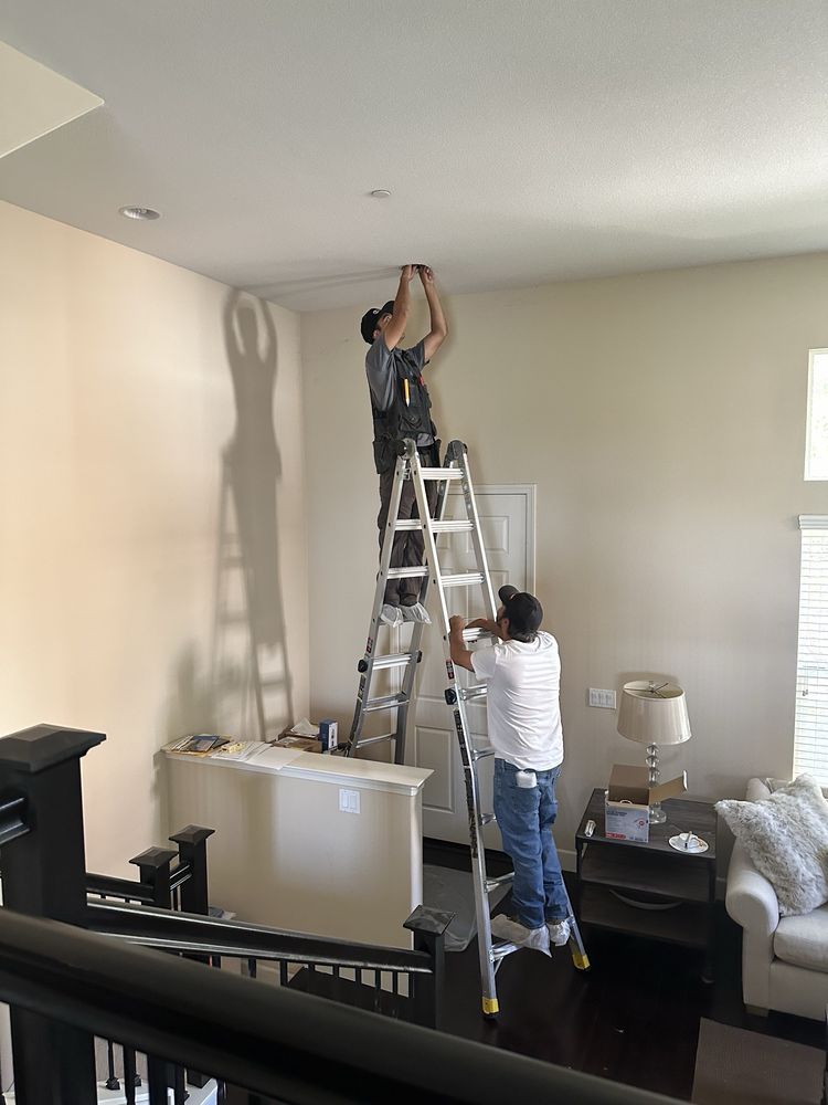 Two Precision Wire electricians on ladders installing recessed ceiling lights in an occupied home.